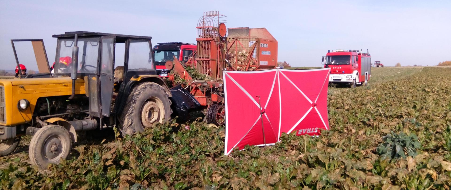 Zdjęcie przedstawia ciągnik rolniczy C-360 z kombajnem do zbioru buraków typ Neptun Z413. W tle widoczne są samochody strażackie.