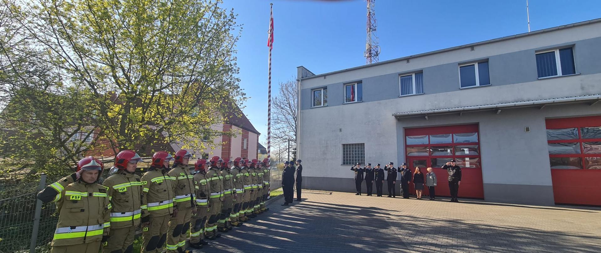 Zdjęcie przedstawia zmiany służbowe, funkcjonariuszy komendy oraz pracowników korpusu służby cywilnej podczas uroczystego podniesienia flagi państwowej.