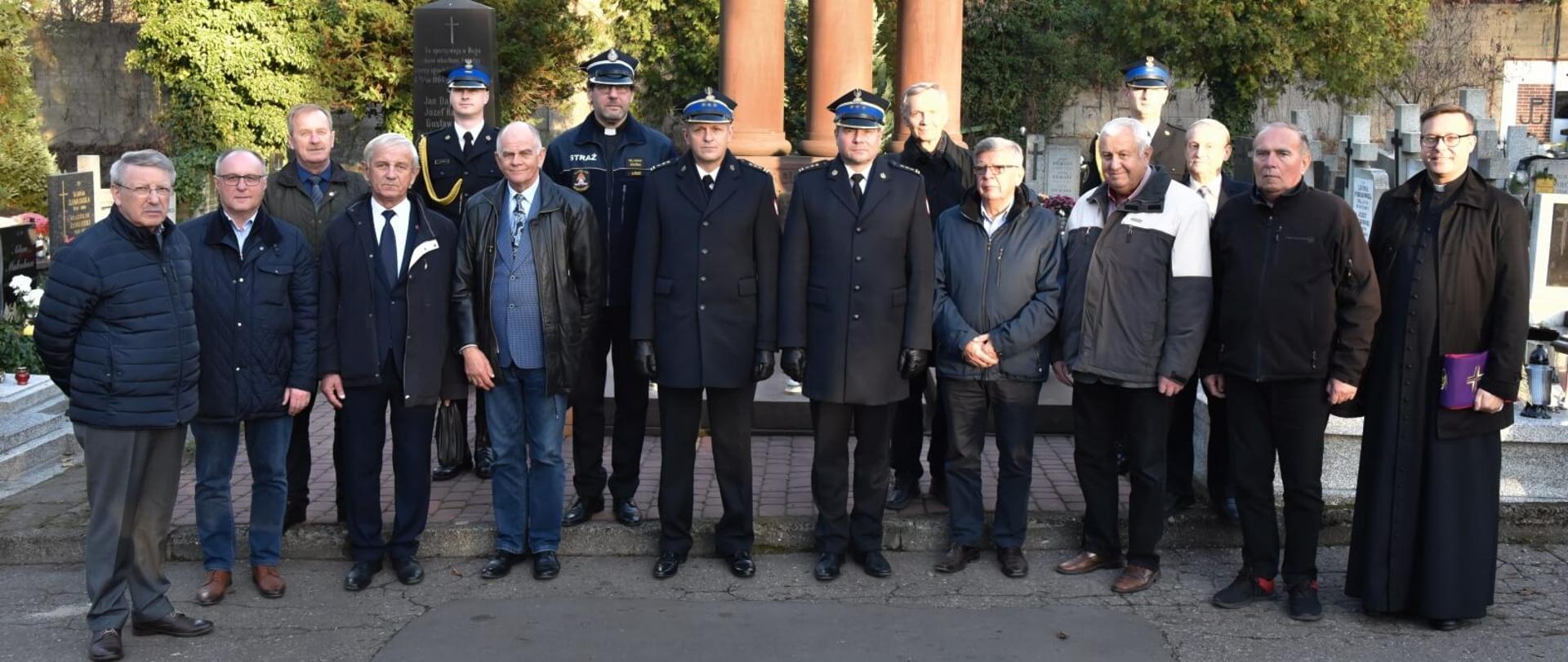 Strażacy PSP, emeryci pożarnictwa, komendanci oraz kapelani pozują do zdjęcia na tle kwatery strażackiej na starym cmentarzu w Łodzi