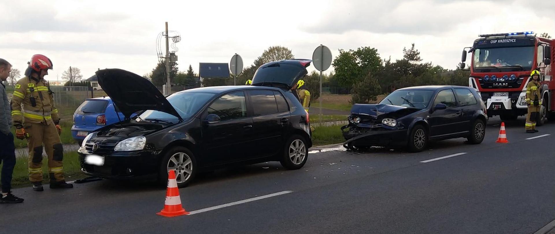 2 uszkodzone samochody osobowe na drodze. W tle samochód strażacki.