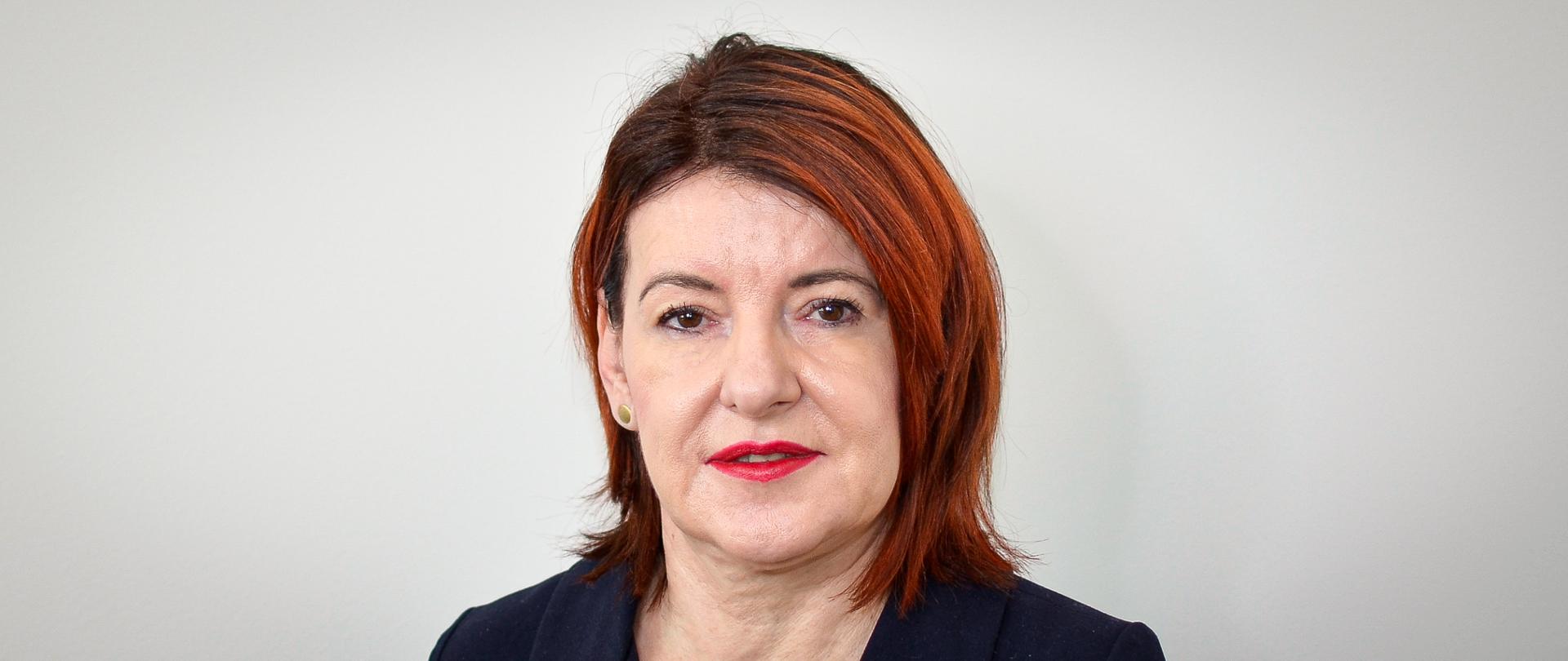 Kobieta w ciemnej marynarce, z kasztanowymi włosami, odsłoniętym jednym uchem