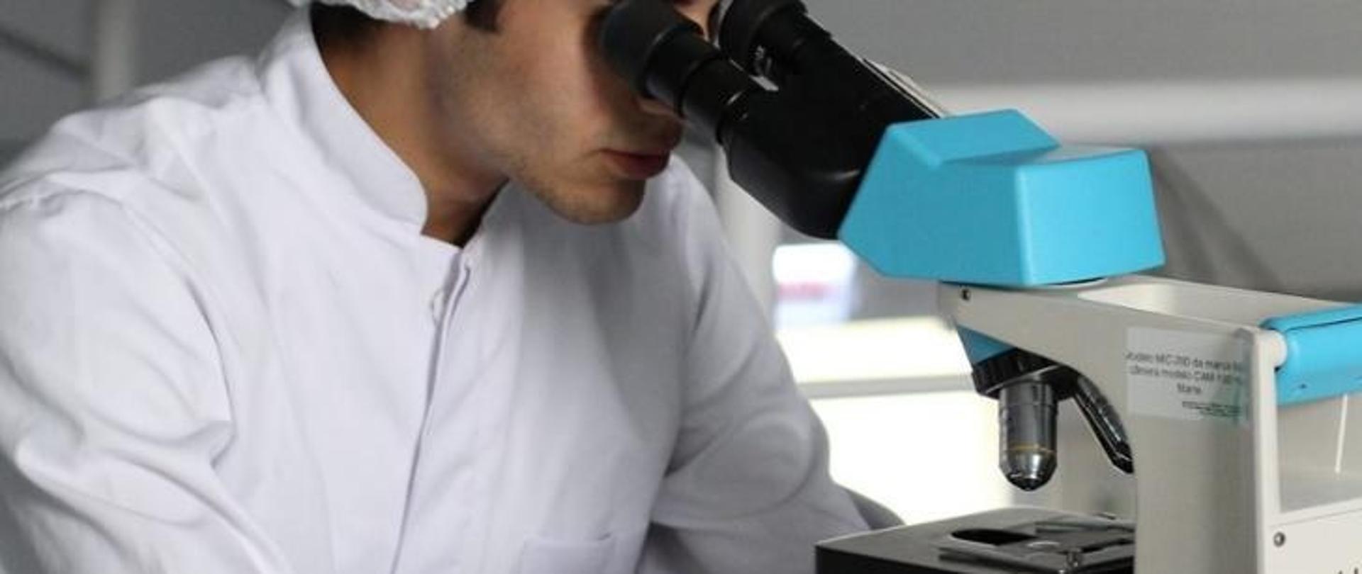 Grafika przedstawia mężczyznę patrzącego przez mikroskop