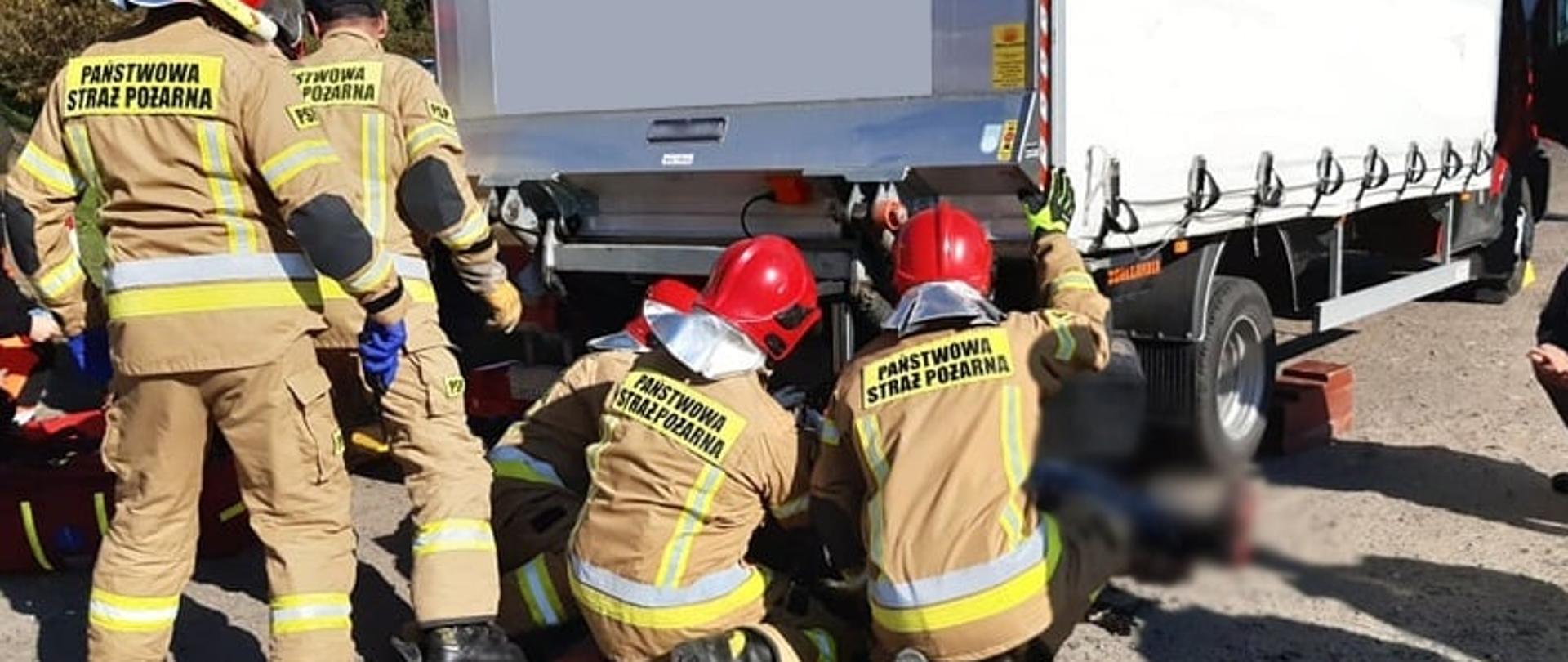 Strażacy w trakcie uwalniania poszkodowanej motocyklistki spod samochodu.