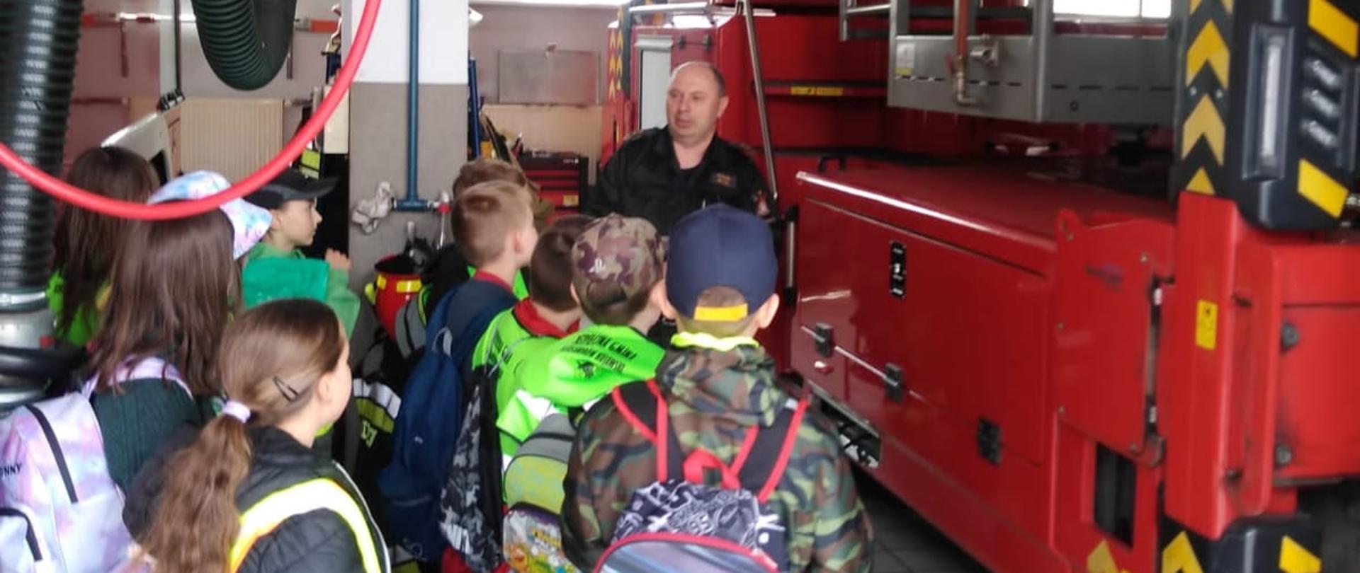Na zdjęciu widać grupkę dzieci stojącą w garażu strażnicy JRG w Ciechocinku , oraz strażaka omawiającego wyposażenie samochodu SCHD 30 . W tle widać pojazd pożarniczy . 