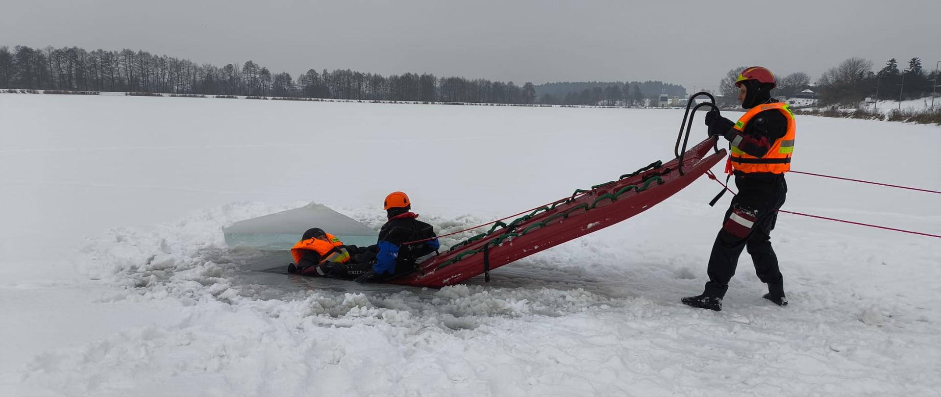 Strażacy ćwiczą ratowanie człowieka , pod którym załamał się lód na zamarźniętym zbiorniku wodnym. 