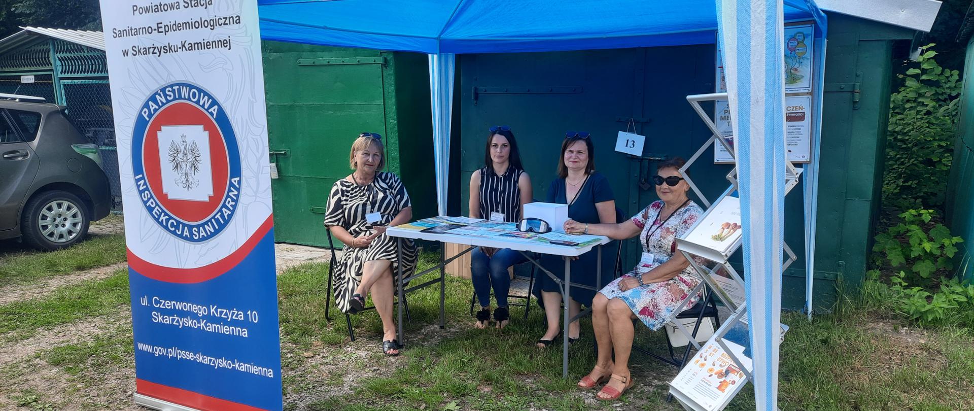 Rozłożony namiot promocyjny pracownicy psse siedzący przy stole z ulotkami