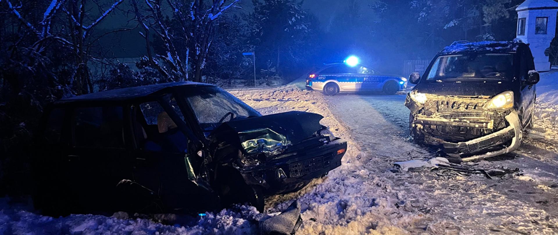 Zdjęcie przedstawia dwa rozbite samochody osobowe na zaśnieżonej drodze.