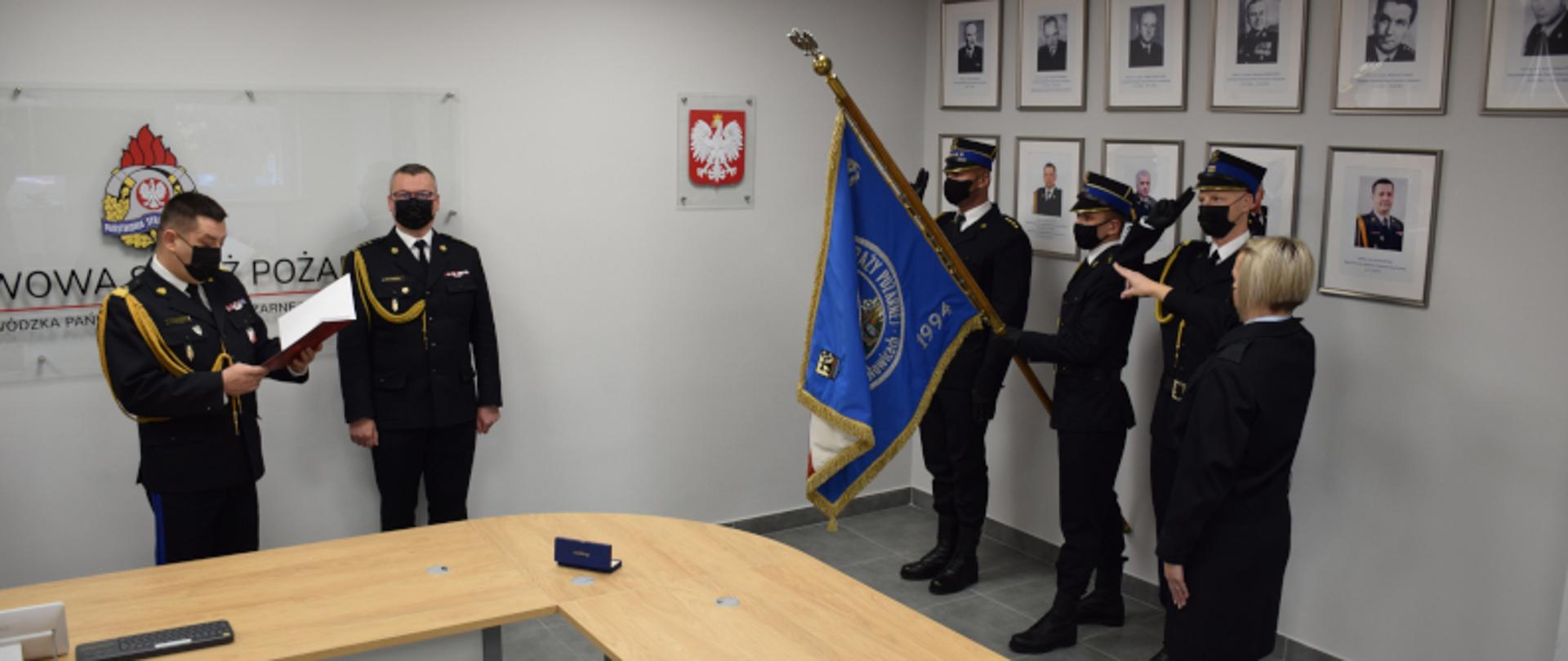 po lewej stronie zdjęcia Śląski Komendant Wojewódzki PSP nadbryg. Jacek Kleszczewski odczytujący strażakowi rotę ślubowania, obok zastępca Śląskiego Komendanta Wojewódzkiego PSP st. bryg. Mirosław Synowiec. Po prawej stronie zdjęcia widoczny poczet sztandarowy Komendy Wojewódzkiej PSP PSP w Katowicach oraz strażak stojący naprzeciwko sztandaru, z uniesioną ręką w kierunku sztandaru