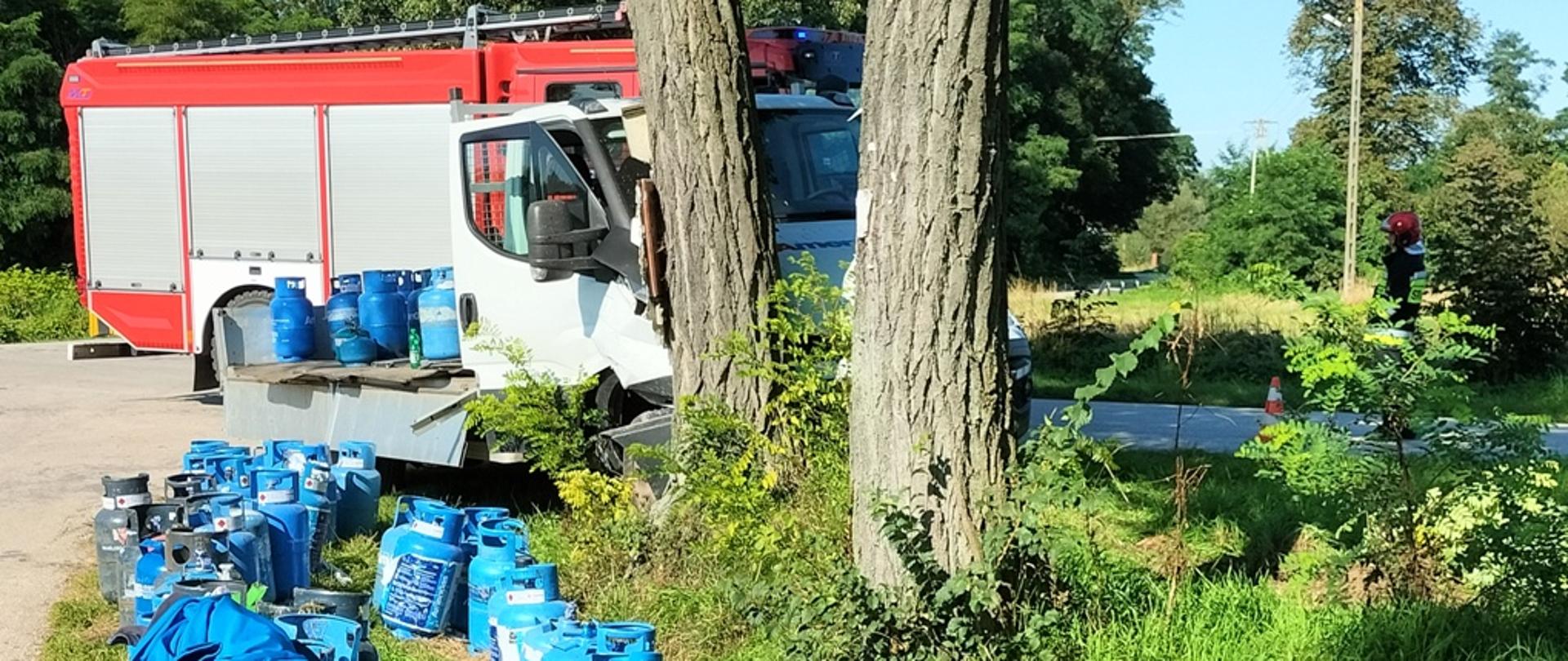 Samochód dostawczy przewożący butle gazowe uderzył w drzewo w tle samochód pożarniczy 