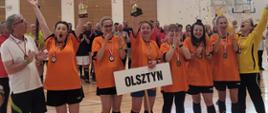 Zwycięska drużyna z Olsztyna celebruje zwycięstwo podnosząc puchar. W tle wystrzelone i opadające, złotem konfetti.