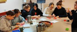 grupa siedmiu dziewcząt siedzi przy stole i wykonuje prace ręczne