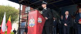 Widok z boku. Trybuna honorowa. Na pierwszym planie prezes Zarządu Oddziału Powiatowego Związku OSP RP w trakcie przemówienia. W tle goście.