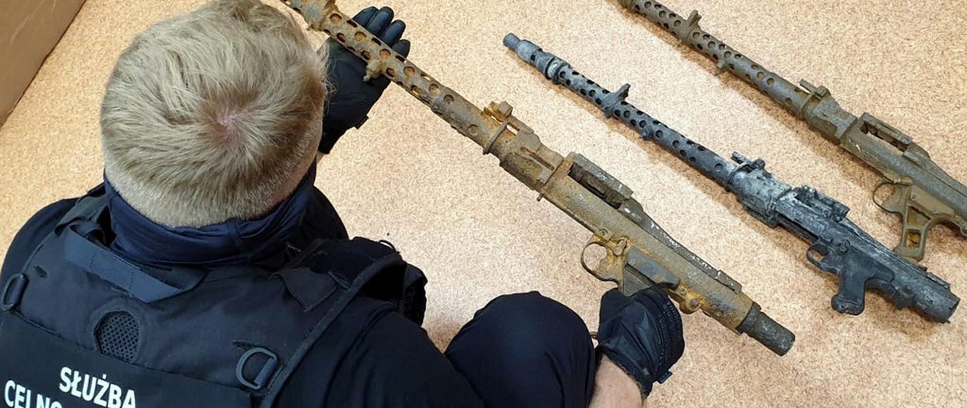 Funkcjonariusz Służby Celno-Skarbowej podczas oględzin ujawnionych karabinów.