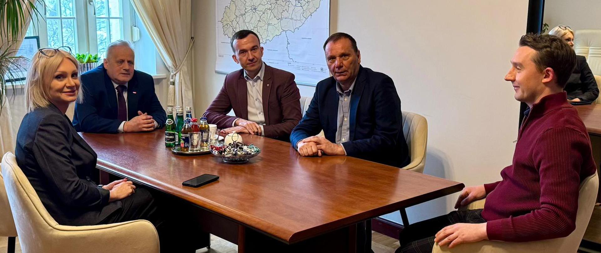 Grupa oficjeli w tym I wicewojewoda, II wojewoda oraz wicemarszałek siedzą przy stole, pozują do zdjęcia 