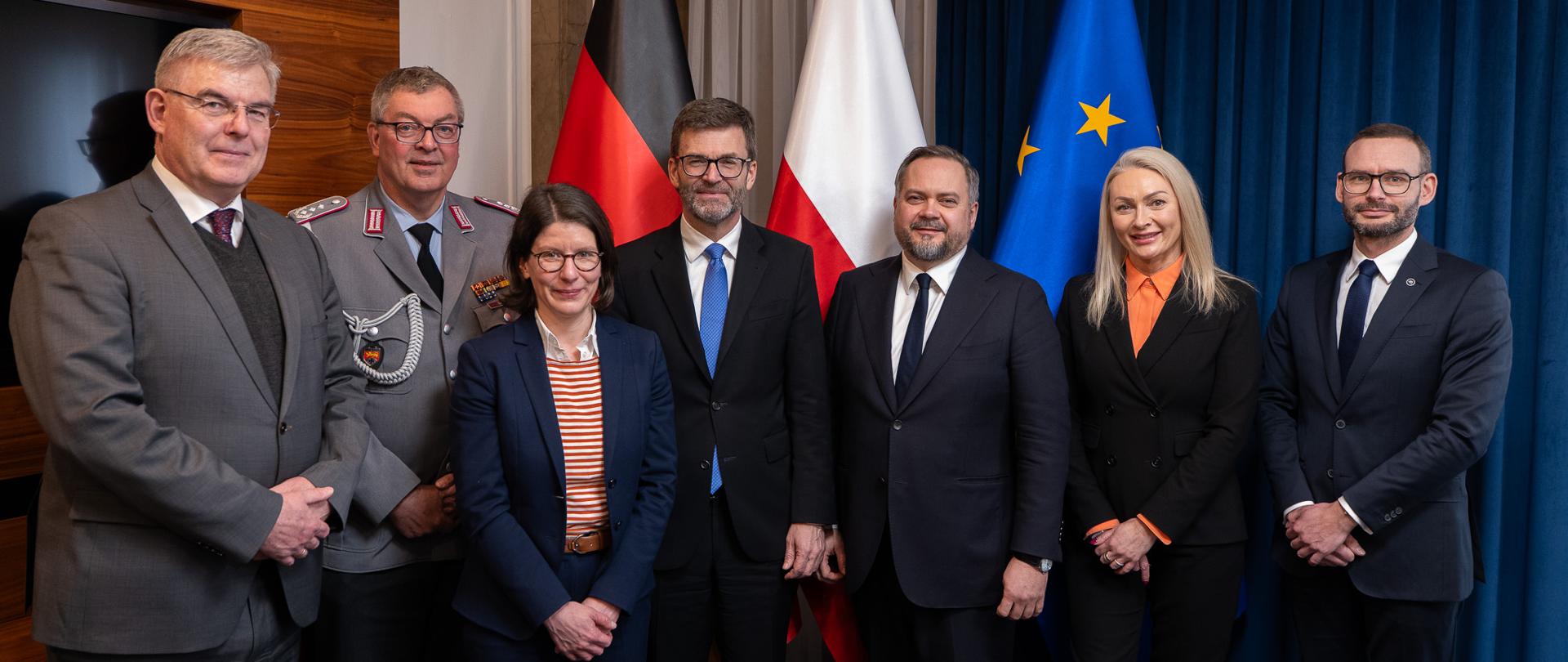 Konrad Gołota, Podsekretarz Stanu w Ministerstwie Aktywów Państwowych, Heiko Thoms, Sekretarz Stanu w Ministerstwie Finansów Republiki Federalnej Niemiec oraz pozostali uczestnicy spotkania stoją na tle flag.