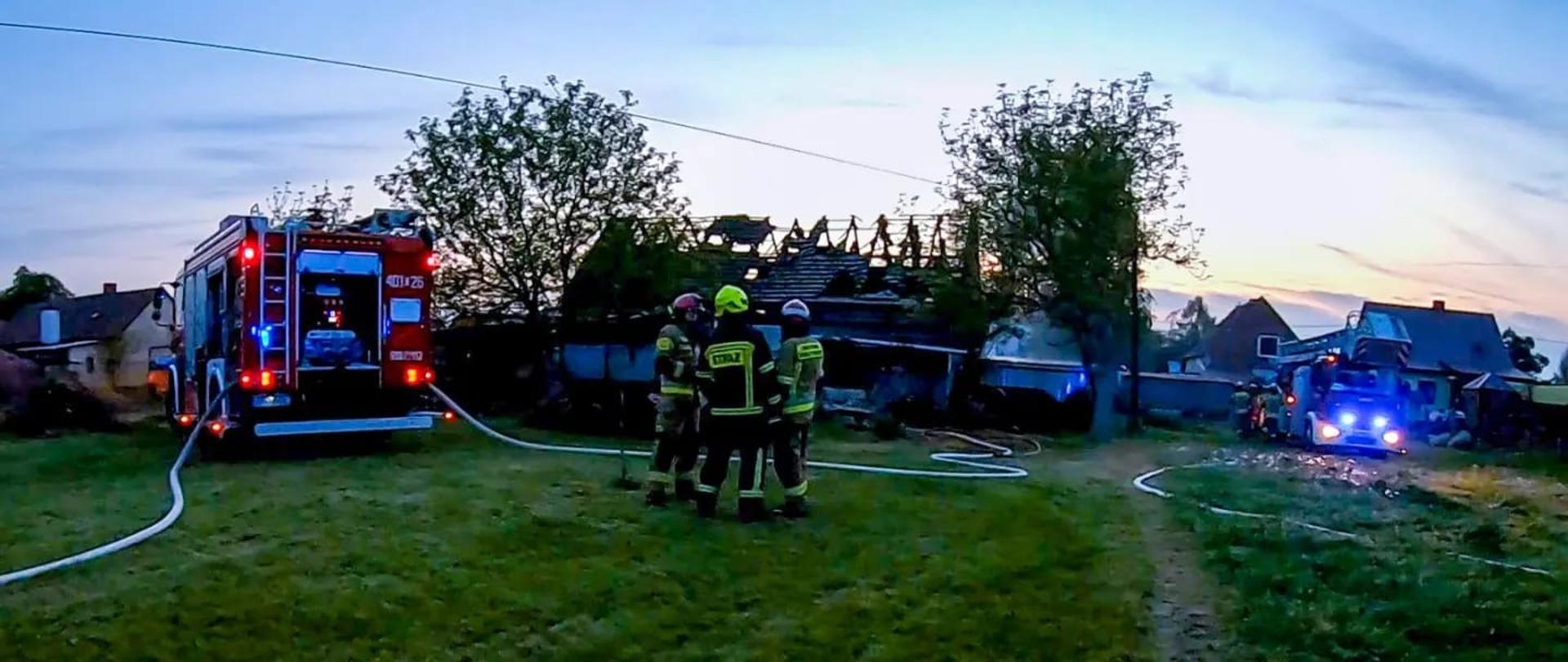 Pożar stodoły w miejscowości Przecza - zdjęcie przedstawia strażaków stojących przed spaloną stodołą, z lewej strony znajduje się samochód gaśniczy