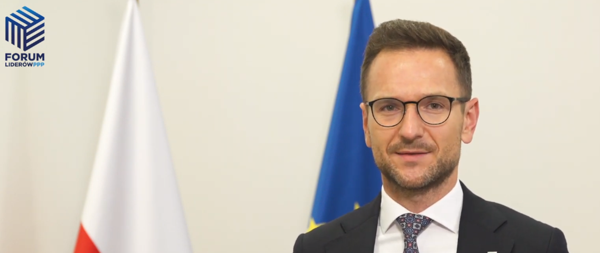 Zdjęcie portretowe wiceministra Waldemara Budy na tle flag Polski i UE. W Lewym górnym rogu logo Forum Liderów PPP.
