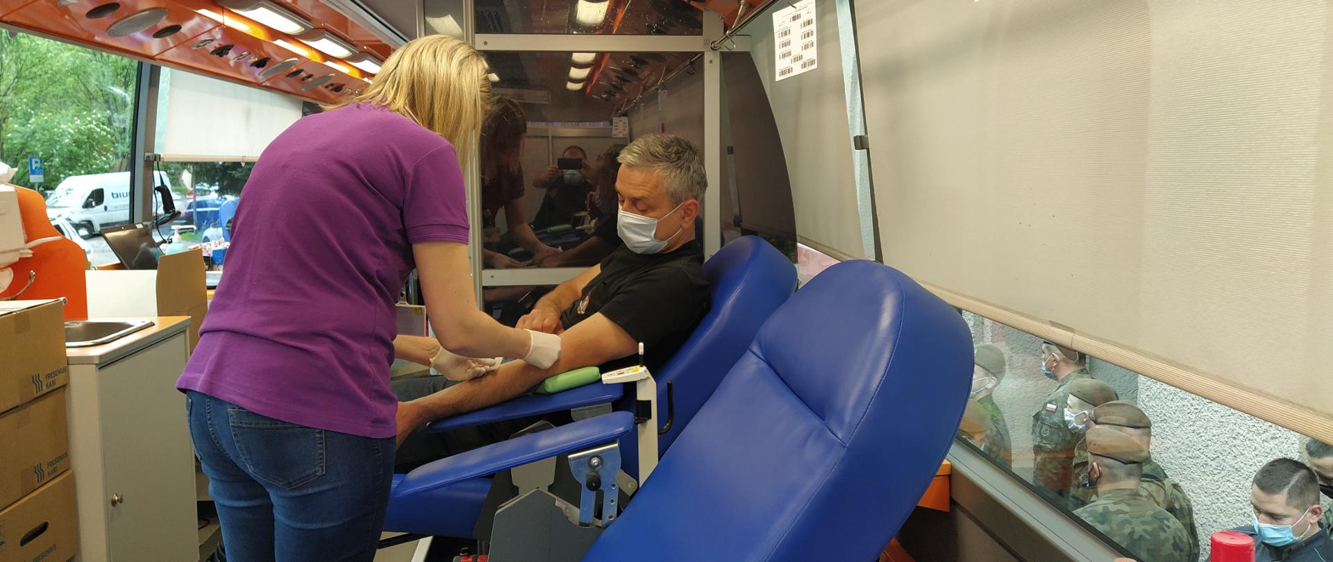 Zdjęcie przedstawia funkcjonariusza Komendy Miejskiej Państwowej Straży Pożarnej w Rzeszowie siedzącego na fotelu podczas oddawania krwi w krwiobusie.