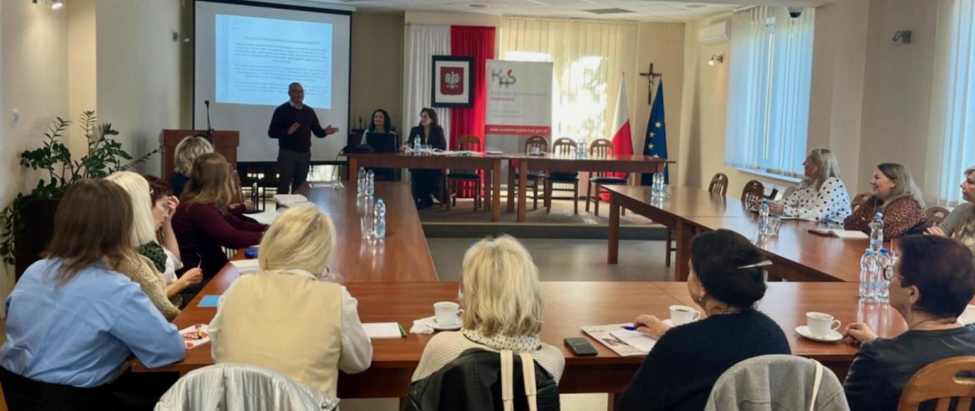 Przy stołach siedzi grupa osób