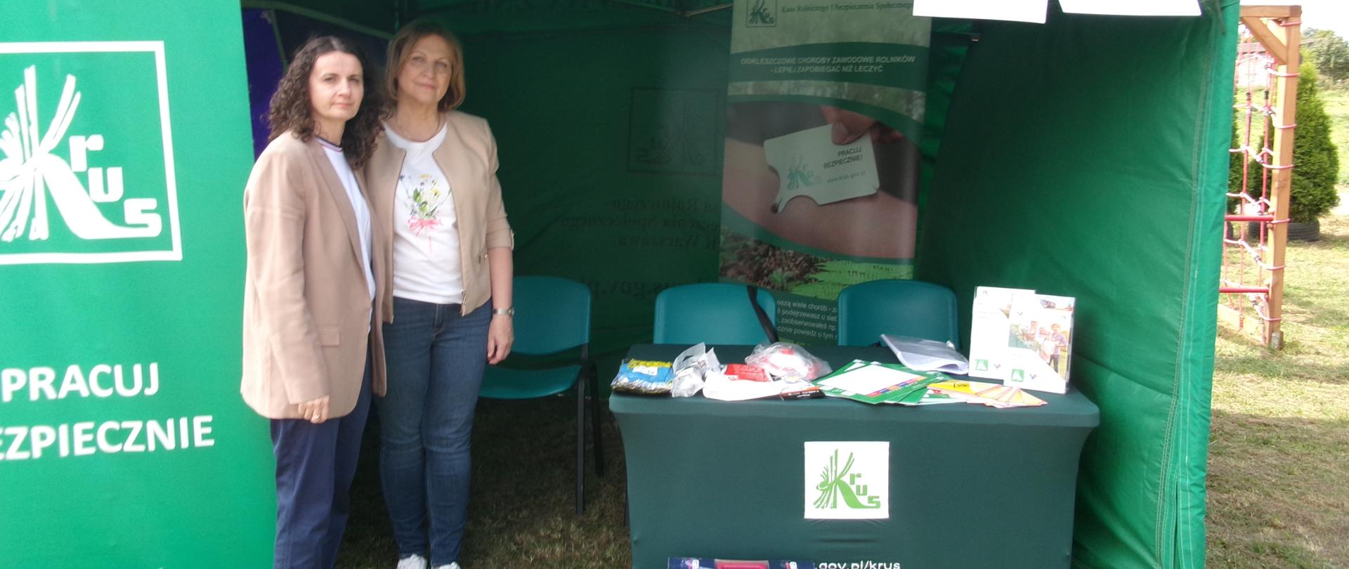 Stoisko KRUS. W centrum zielony namiot opatrzony hasłem: „Pracuj Bezpiecznie”. Po lewej baner z logiem Kasy. Pod namiotem stoliki wyłożone broszurami i materiałami prewencyjnymi. Po lewej pracownicy KRUS.