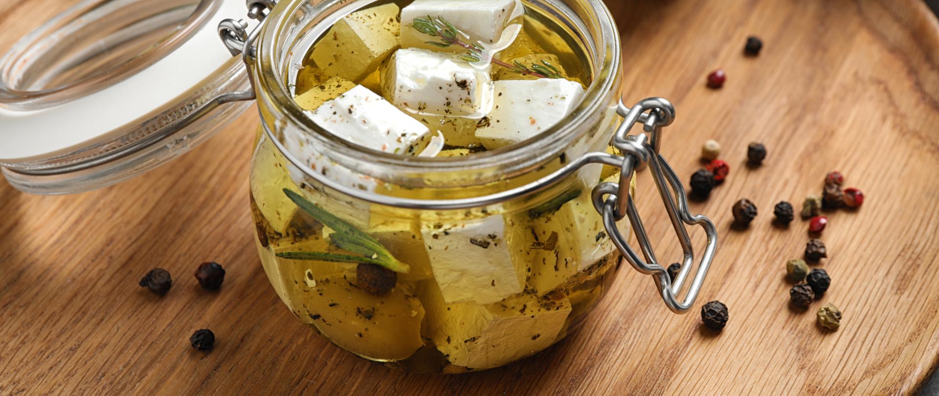 Jar with feta cheese marinated in oil on table. Pickled food