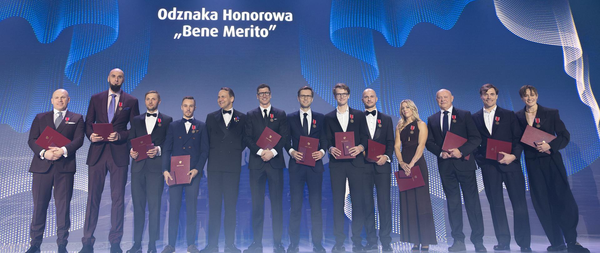 13 people on stage in formal clothing presenting diplomas and Bene Merito honorary distinctions to outstanding athletes