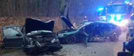 kadr przedstawia drogę w lesie, na środku pasa dwa rozbite auta, za wrakami widać strażaka i wóz straży pożarnej