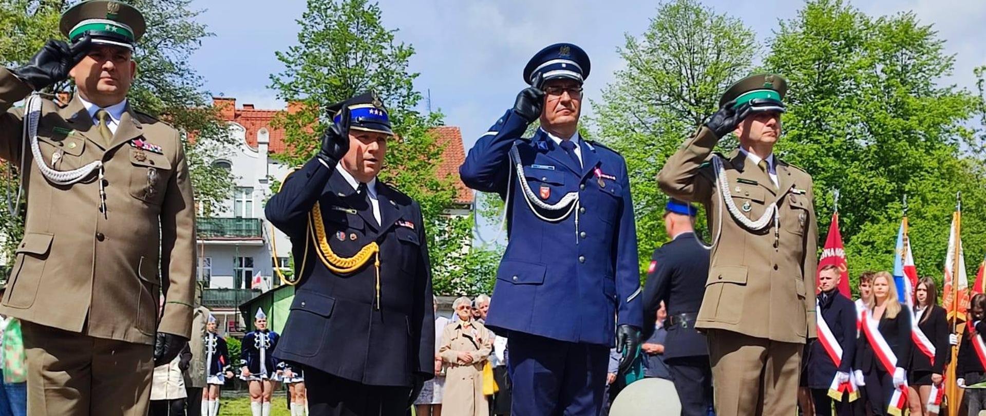 Na zdjęciu czterech funkcjonariuszy służb mundurowych salutują przy składaniu kwiatów. Słonecznie.