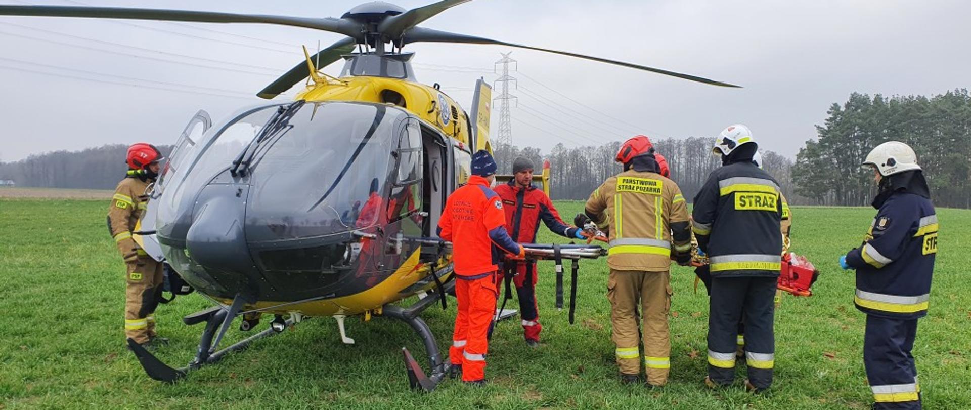 Śmigłowiec LPR przy którym stoi personel lotniczy i strażacy.