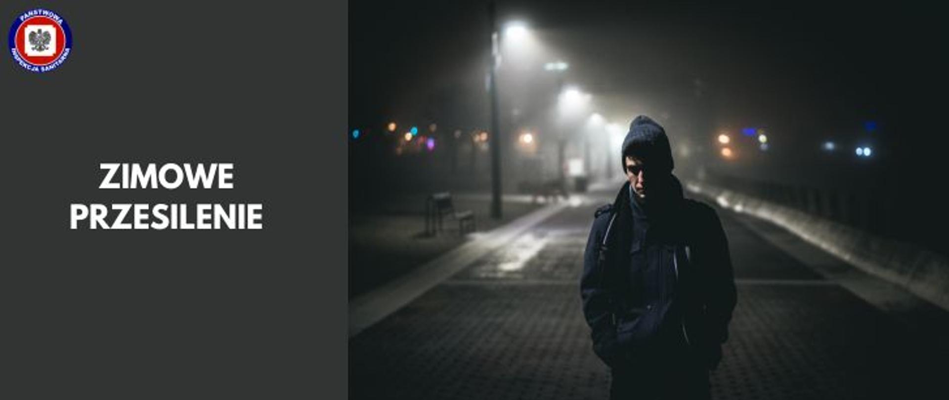 Po lewej na ciemnoszarym tle jasny napis zimowe przesilenie, w lewym górnym rogu logo Państwowej Inspekcji Sanitarnej. Po prawej młody mężczyzna nocą stoi na ulicy w zimowym ubraniu.