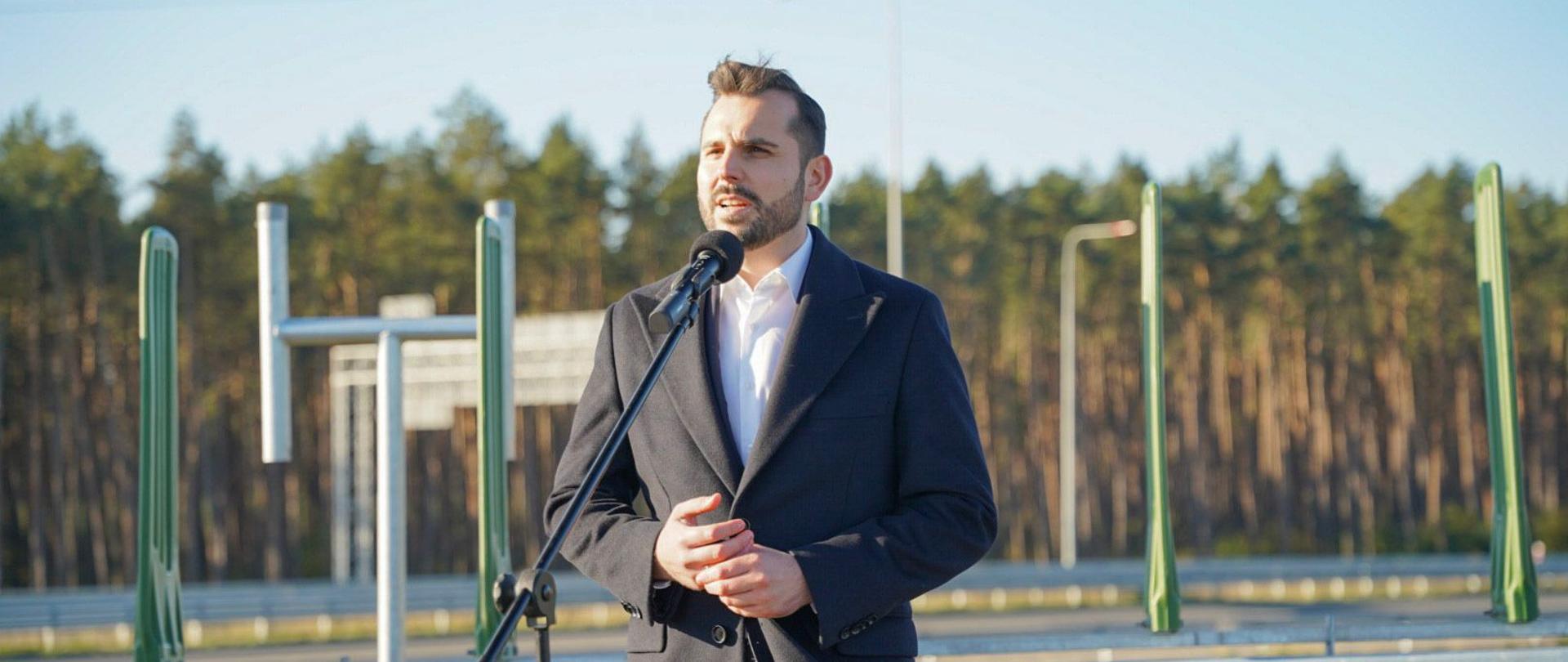 wicewojewoda Bartosz Brożyński przy mikrofonie, na tle drogi