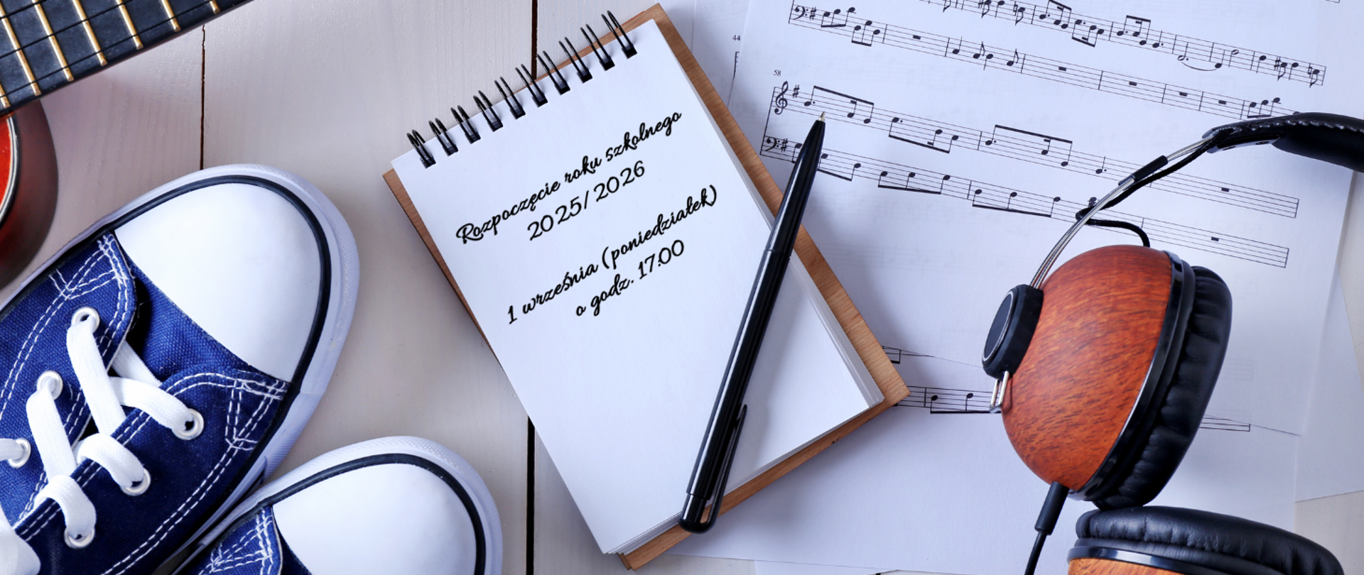 Baner w jasnej, pastelowej kolorystyce z elementami w odcieniach granatu, bieli, czerni i drewna. Na środku widoczny jest notatnik z czarnym długopisem, na którym umieszczony jest napis:
„Rozpoczęcie roku szkolnego 2025/2026
1 września (poniedziałek) o godz. 17.00”.
Wokół notatnika znajdują się: granatowe trampki z białymi sznurówkami, gitara, drewniane słuchawki nausznie oraz nuty wydrukowane na kartkach. Całość tworzy nowoczesną, młodzieżową i muzyczną atmosferę baneru.