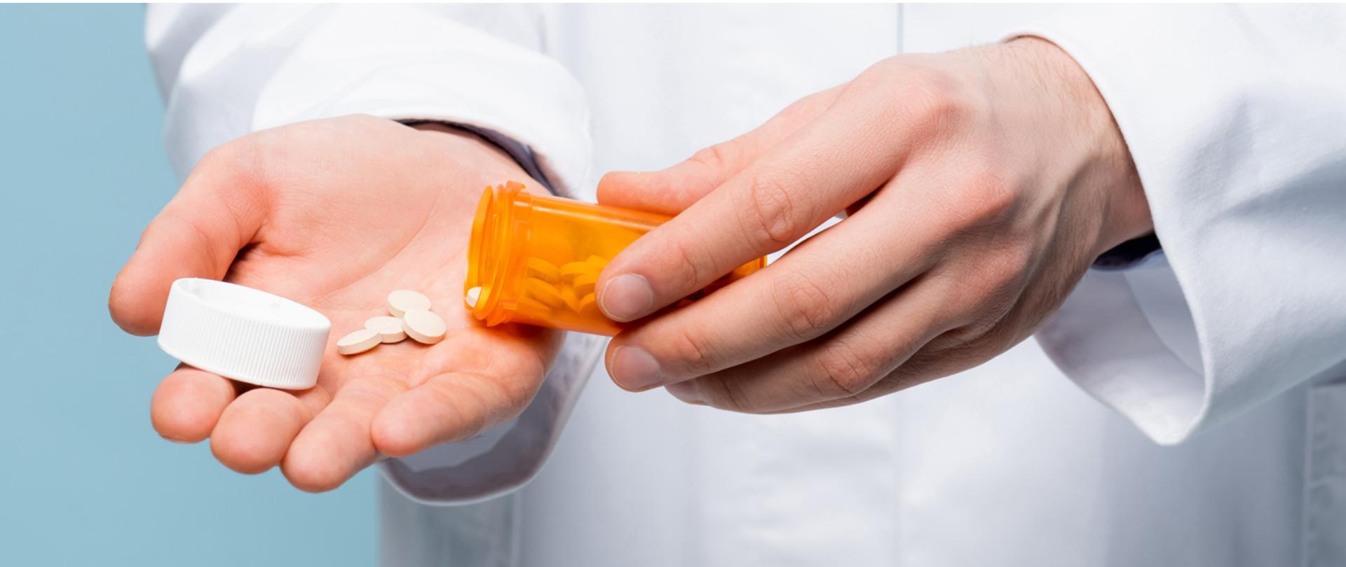 Na zdjęciu są widoczne dłonie mężczyzny. Z jednej na drugą wysypuje tabletki z plastikowego opakowania.