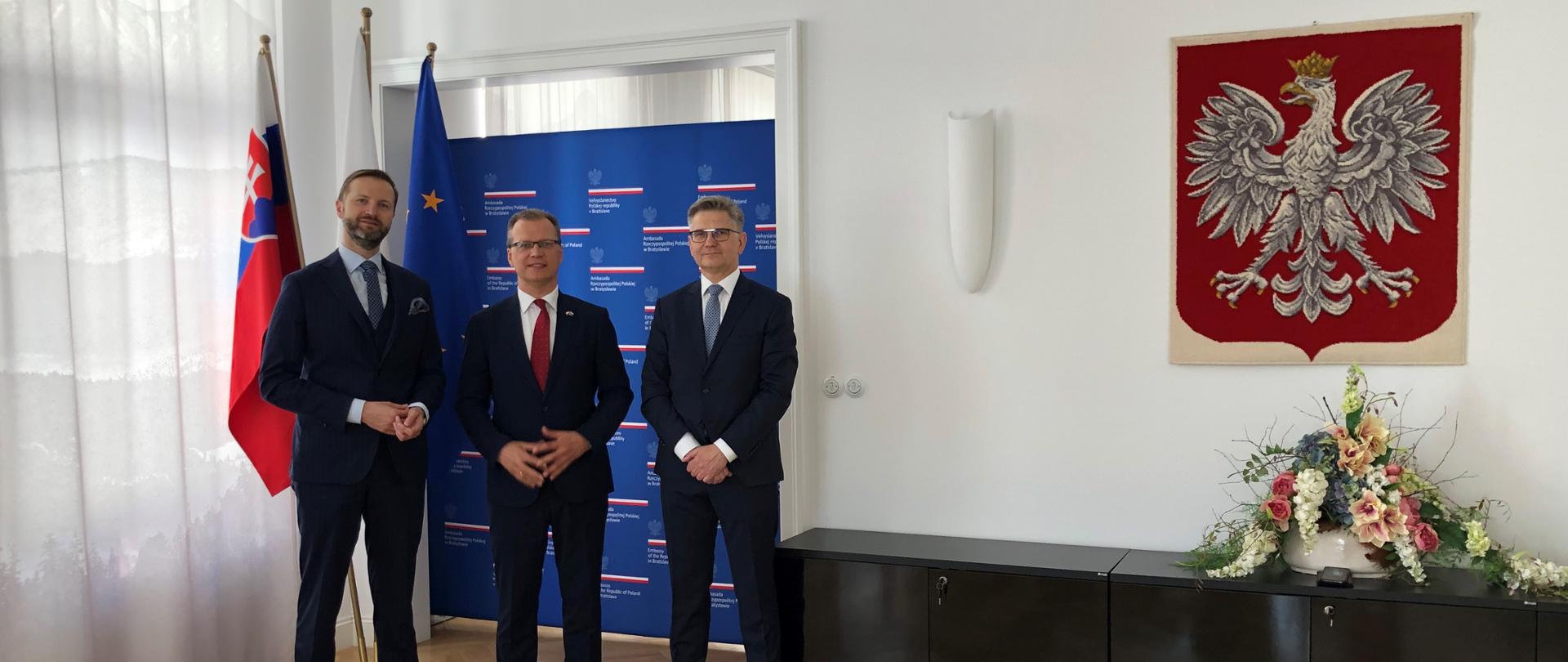 Tomasz Wiatrak, Marek Gieroń i ambasador Krzysztof Strzałka stoją na tle flag Polski, Słowacji i UE