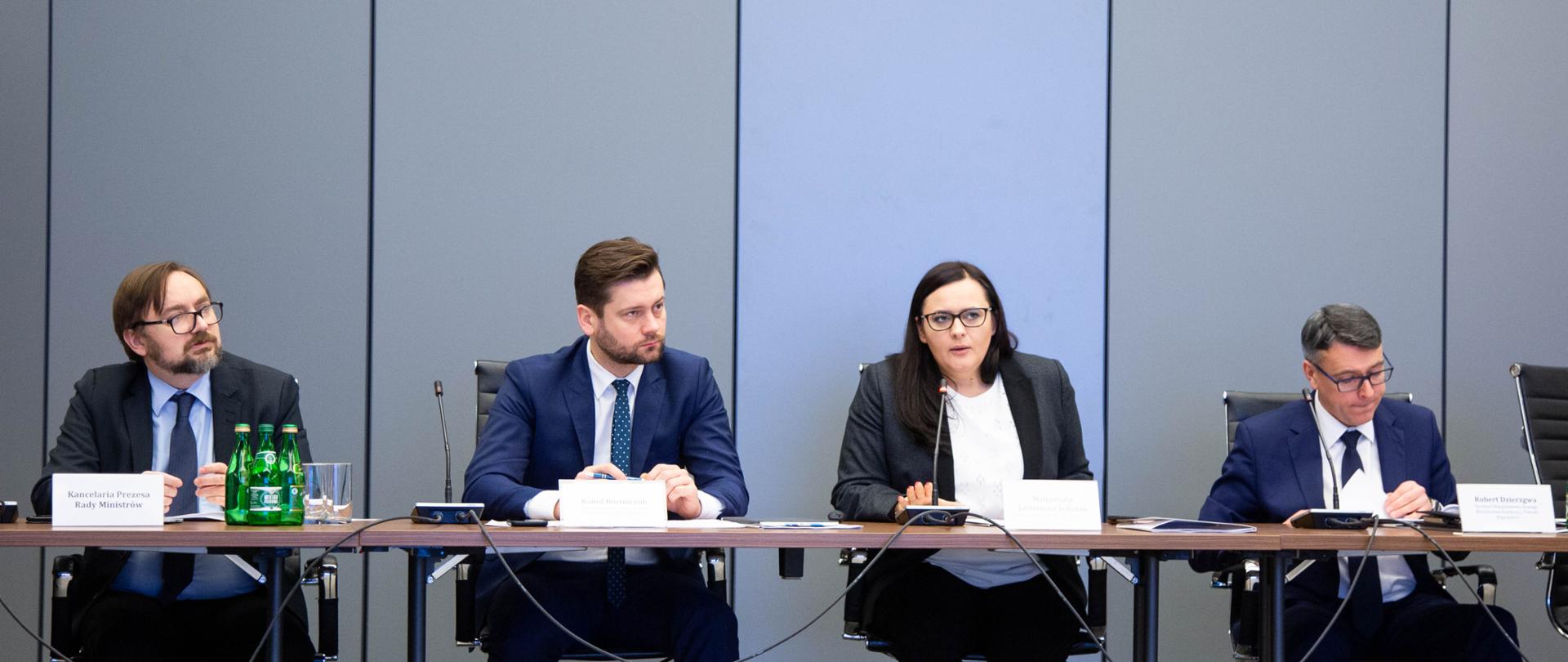 przy stole siedzą paneliści, wśród nich minister Małgorzata Jarosińska-Jedynak, która mówi do mikrofonu i wiceminister Kamil Bortniczuk