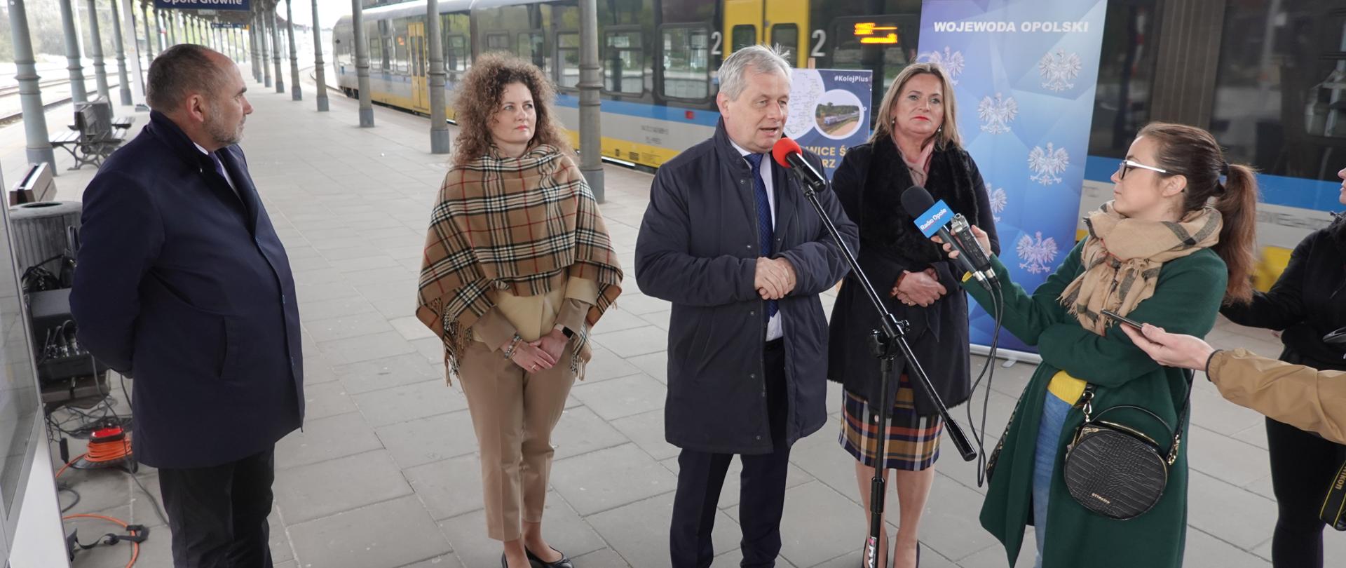 Na zdjęciu Wojewoda Opolski wraz z gośćmi. Zdjęcie wykonane na dworcu kolejowym. Osoby stoją na peronie, w tle pędzący pociąg 