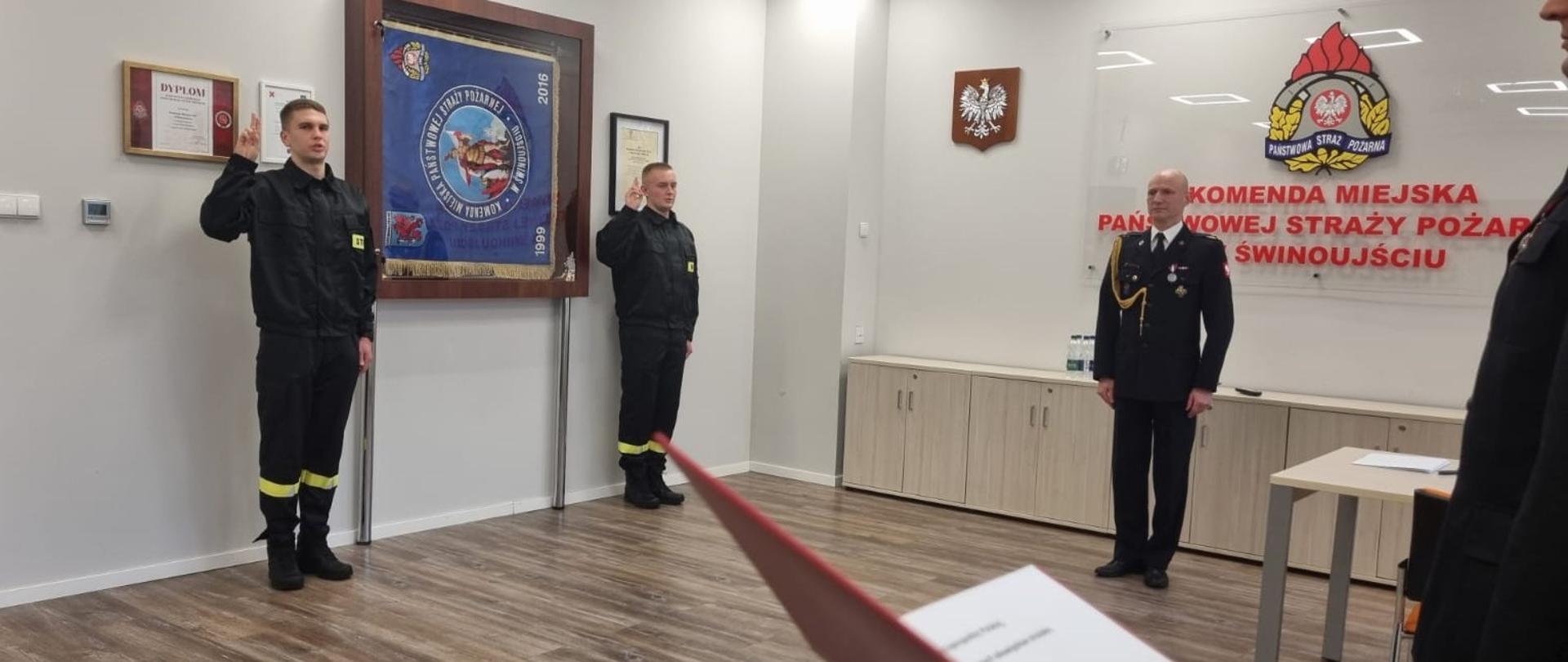 Zdjęcie przedstawia strażaków na tle witryny ze sztandarem KM PSP w Świnoujściu