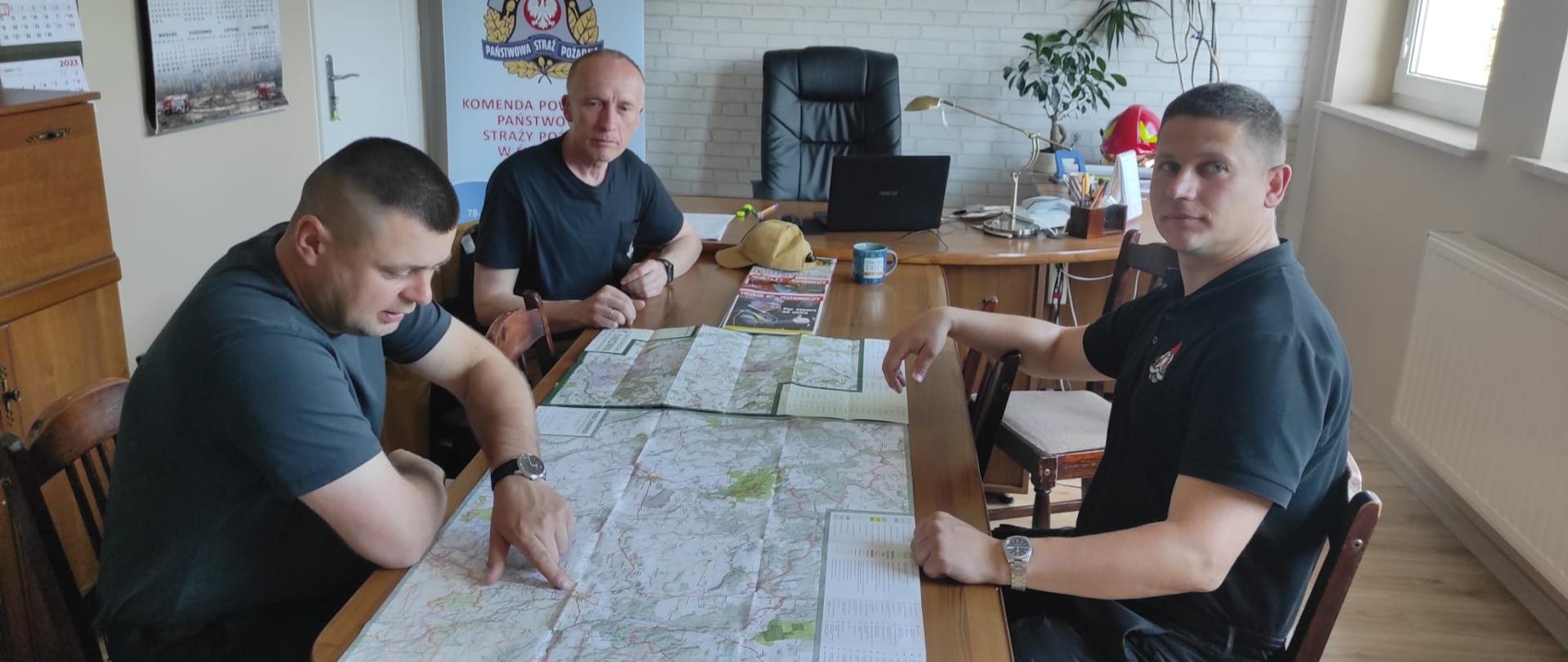 Zdjęcie przedstawia trzech mężczyzn siedzących przy stole na którym są mapy.