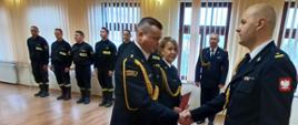 Funkcjonariusze stoją na sali w KP. Komendanta wręcza awanse 2 funkcjonariuszom. 