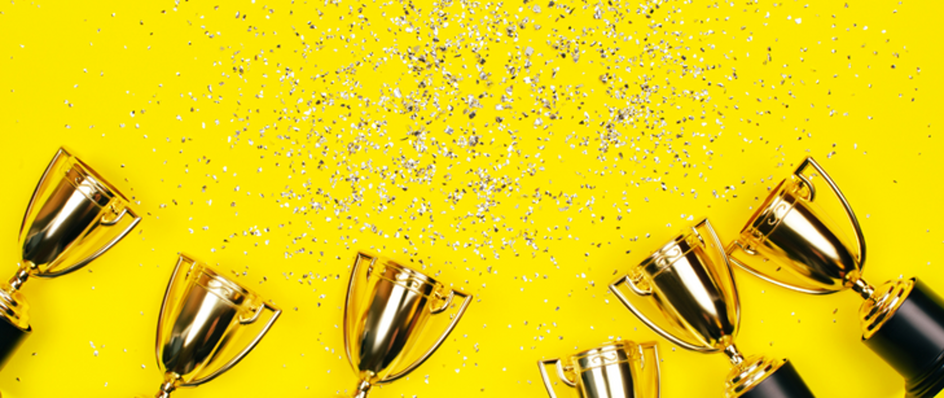 logo zakładki: osiągnięcia uczniów, przedstawia 6 złotych pucharów na żółtym tle z wirującym konfetti nad nimi