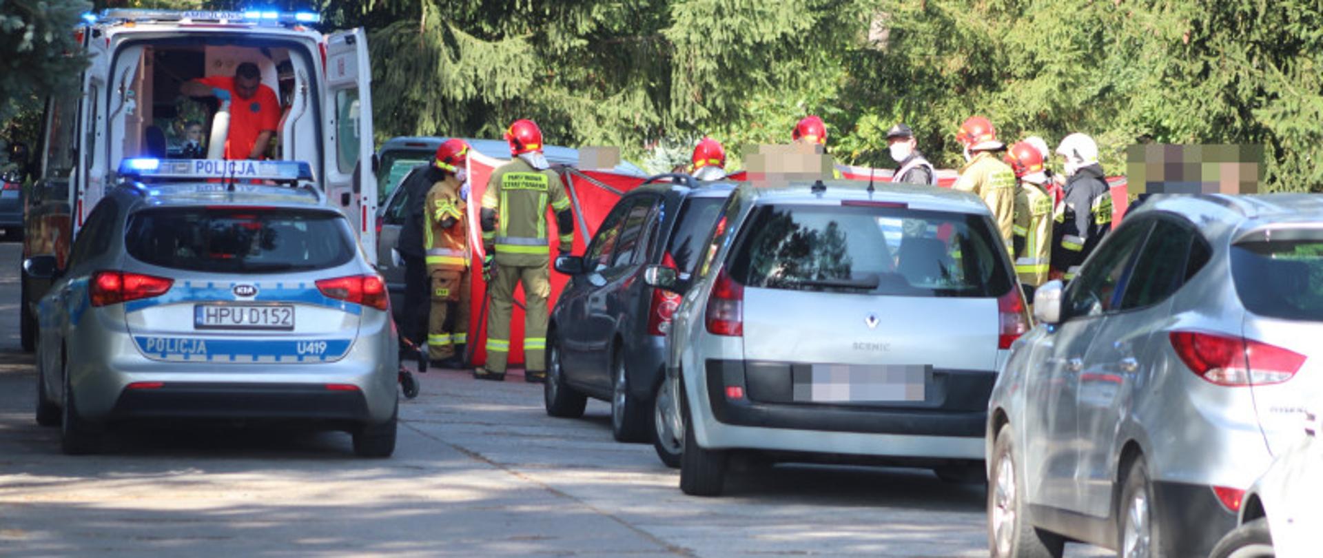 Zdjęcie przedstawia samochody osobowe. W tle stoją: patrol Policji, karetka oraz strażacy udzielający pomocy medycznej.