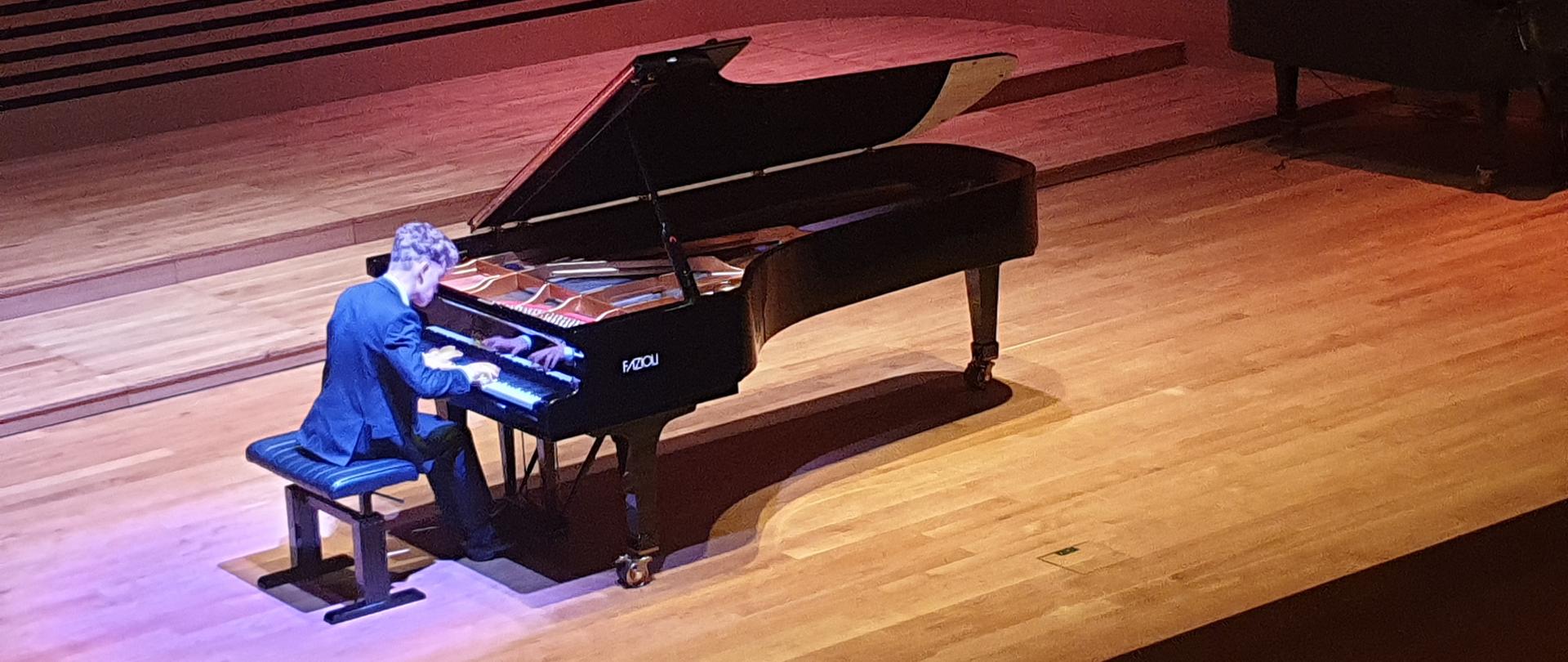 Młody mężczyzna gra na fortepianie na scenie sali koncertowej PSM