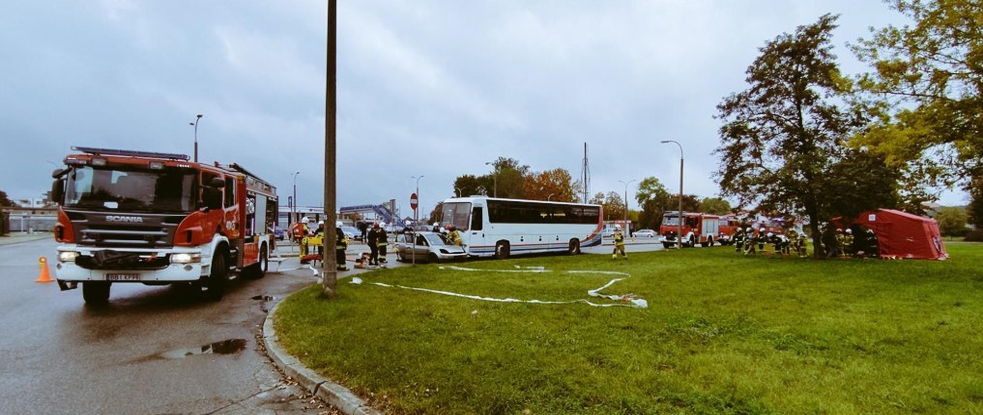 Teren ćwiczeń strażackich. w centralnej części autokar i samochód osobowy po zderzeniu. Obok samochody ratowniczo-gaśnicze oraz namiot strażacki, w którym zorganizowano punkt udzielania pomocy medycznej.