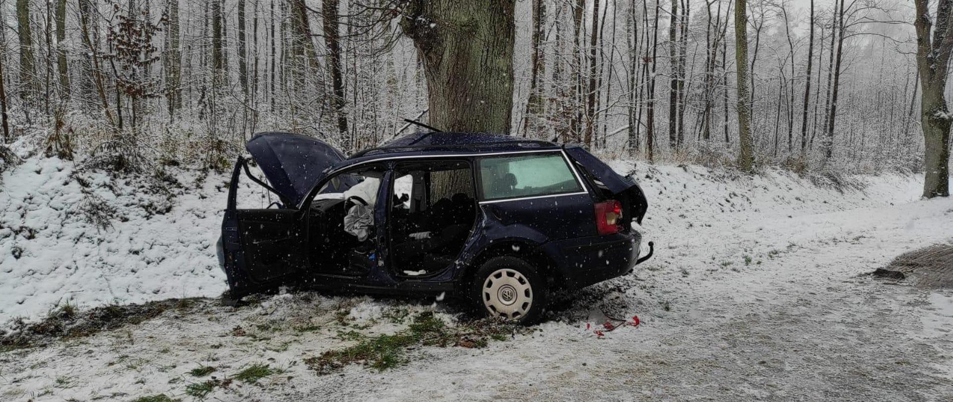 Na poboczu drogi stoi auto, niebieskie kombi, które uderzyło bokiem prawym w drzewo. Biało od śniegu.