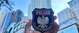 na tle wieżowców Chicago, Emblemat z umundurowania strażaka z napisem POLAND POLISH ASSISTANCE oraz wizerunkiem Orła - Godła RP