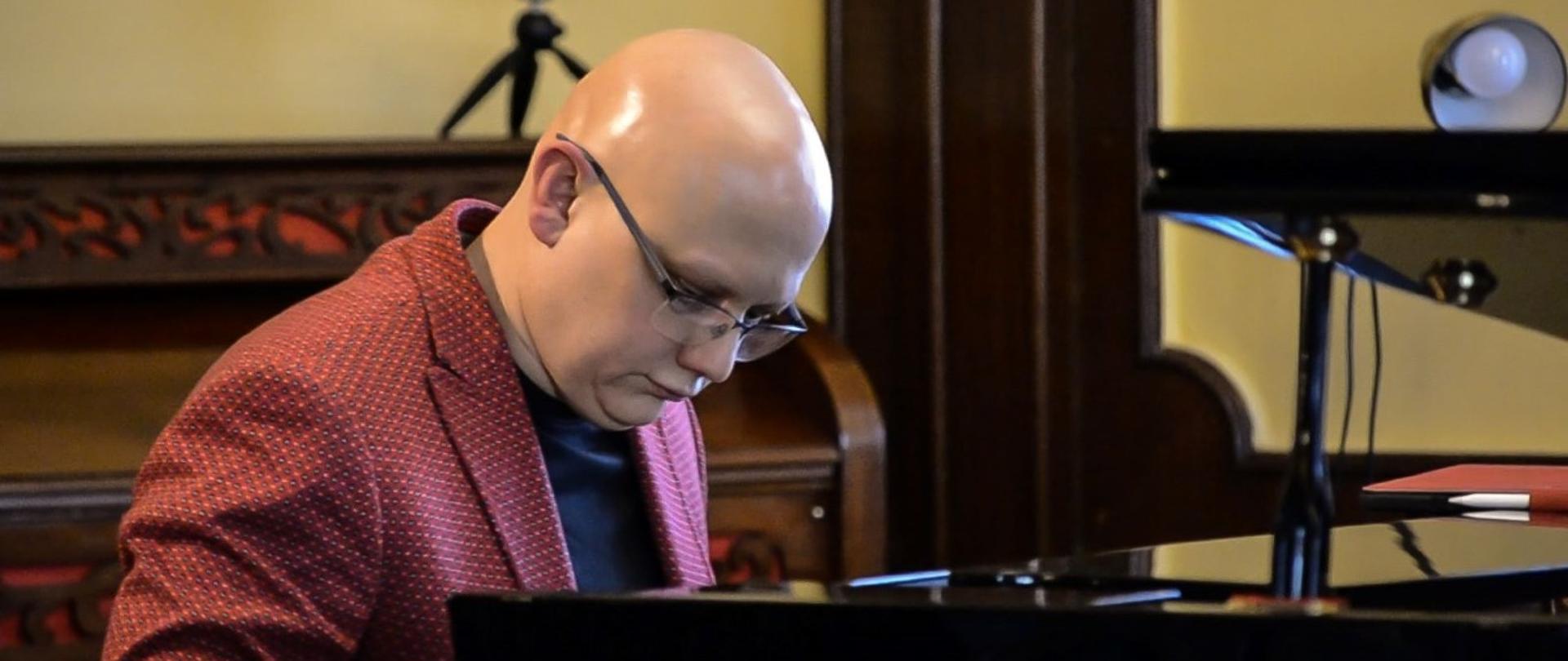 Zdjęcie kolorowe. Muzyk siedzi przy fortepianie podczas koncertu wykonując swoją partię solową. 