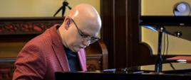 Zdjęcie kolorowe. Muzyk siedzi przy fortepianie podczas koncertu wykonując swoją partię solową. 