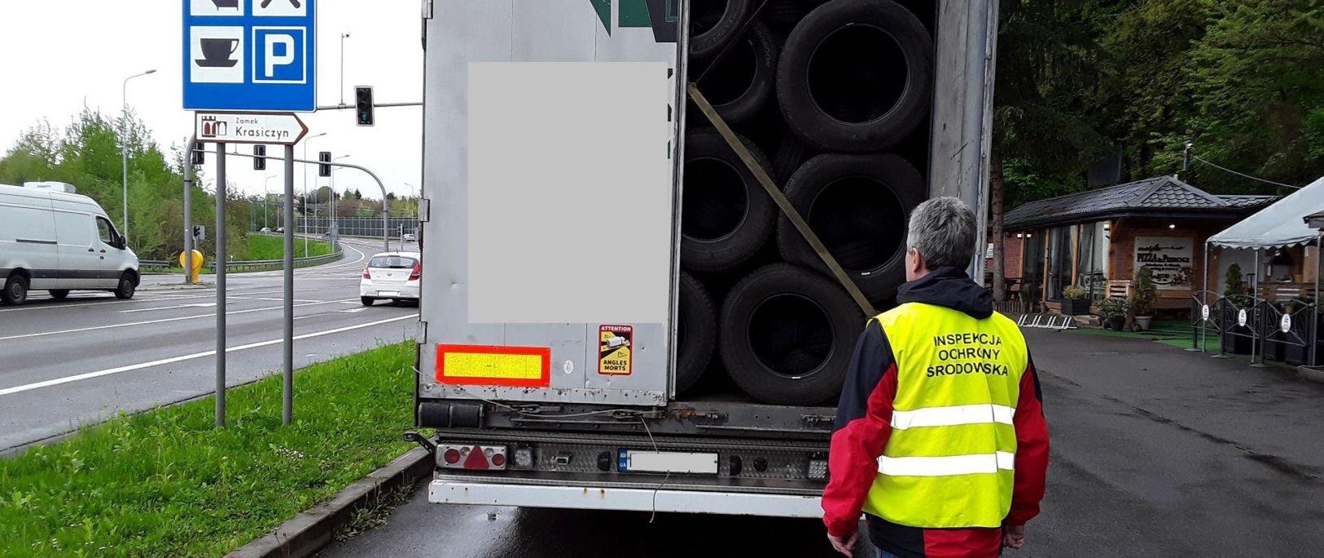 Inspektor IOŚ stojący na tle tyłu ciężarówki z otwartymi drzwiami i widocznym ładunkiem opon.