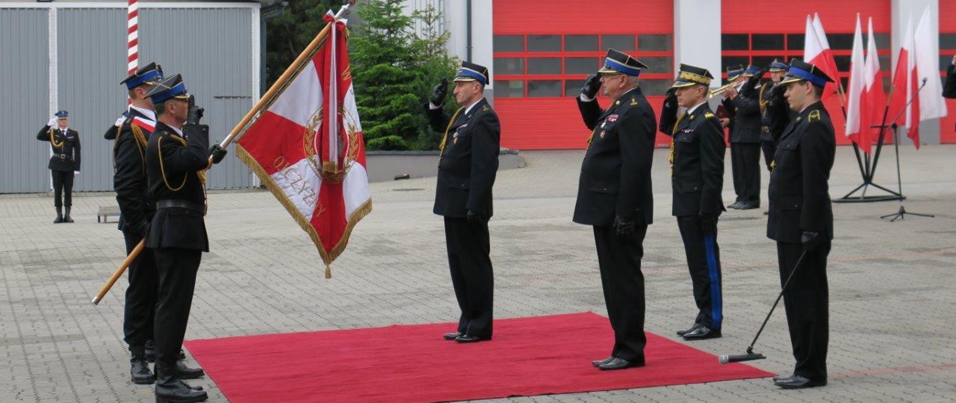 Powołanie małopolskiego komendanta wojewódzkiego PSP – na zdjęciu strażacy salutują do sztandaru. Na drugim planie budynek komendy i drzwi garaży strażackich.