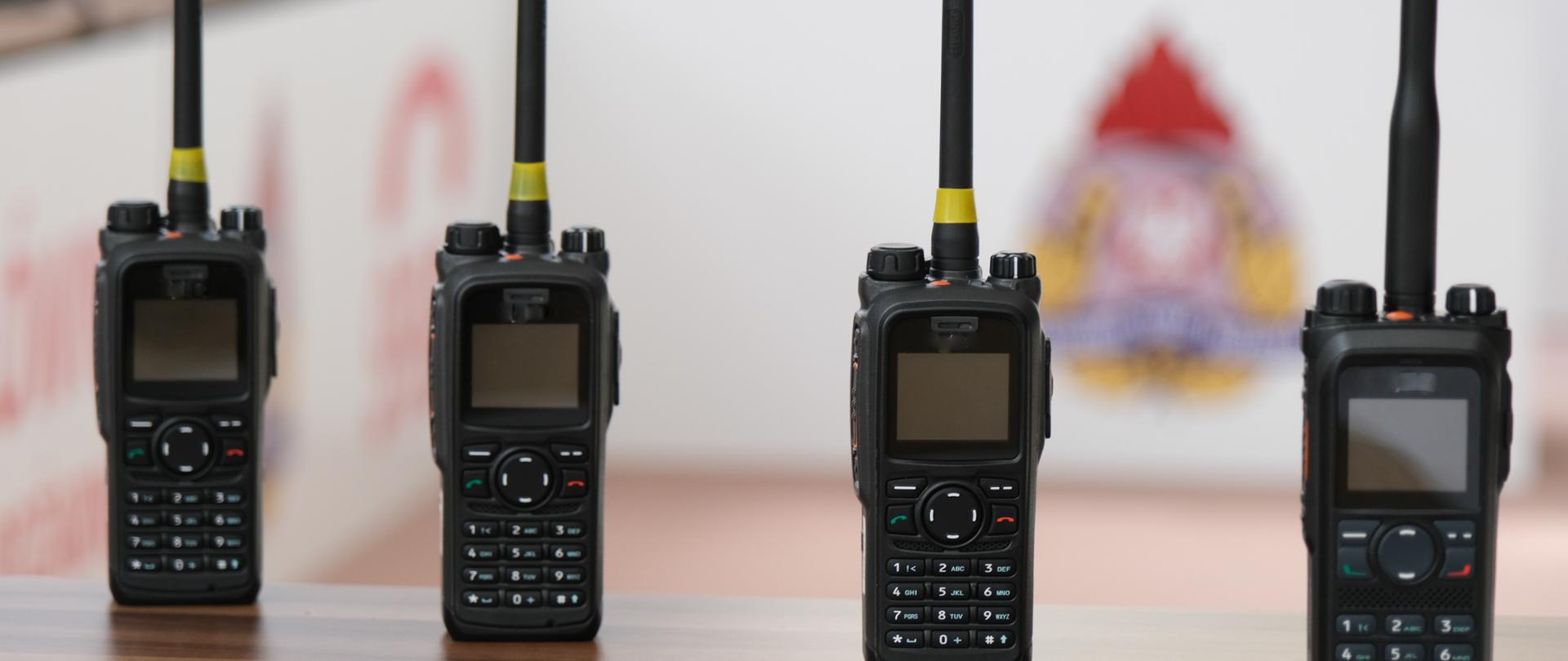 Na zdjęciu widać cztery radiotelefony koloru czarnego, w tle rozmyty logotyp PSP.